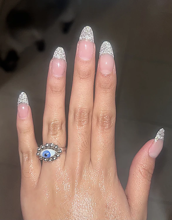 Uñas almendradas largas, nude con puntas de glitter plateado, y anillo de ojo turco