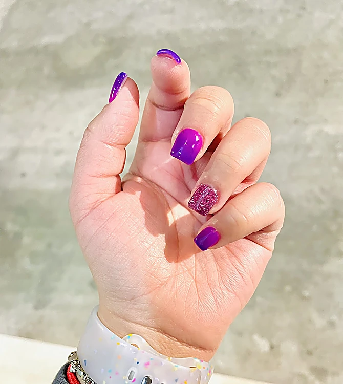 Uñas cortas moradas con una uña de glitter morado