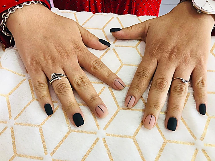 Dos manos sobre una toalla blanca con uñas en negro mate y nude alternadas
